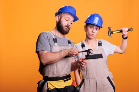 Photo for Confident constructors holding renovating tools on camera, using sledgehammer and pair of pliers to work on renovation project. Builders team posing with hammer and pliers over background. - Royalty Free Image