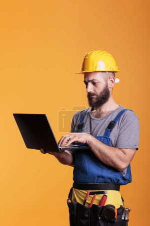Photo for Young renovator using laptop to browse internet website, looking for renovating inspiration. Construction site expert holding portable pc with wireless network, constructor at engineering job. - Royalty Free Image