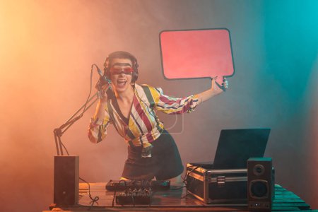Photo for Happy artist holding speech bubble with cardboard paper to advertise message on isolated mockup template. Woman DJ using billboard to show icon, mixing techno music in studio with smoke. - Royalty Free Image