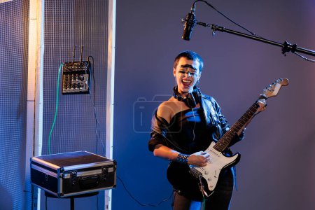 Photo for Cool guitarist singing heavy metal music and screaming loud in studio, using bass guitar to play alternative rock. Female singer doing live performance with leather jacket, playing instrument. - Royalty Free Image