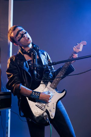 Foto de Estrella del rock tocando guitarra en vivo, sintiendo música heavy metal y disfrutando del punk rock alternativo. Cool artista funky utilizando el instrumento y el canto, usando chaqueta de cuero. - Imagen libre de derechos
