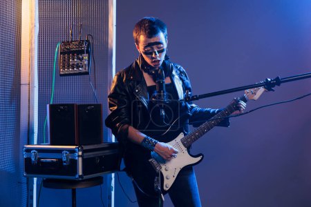 Photo for Musical artist with crazy make up playing guitar, singing alternative rock and heavy metal music in studio with smoke. Talented rocker wearing leather jacket and performing with instrument. - Royalty Free Image