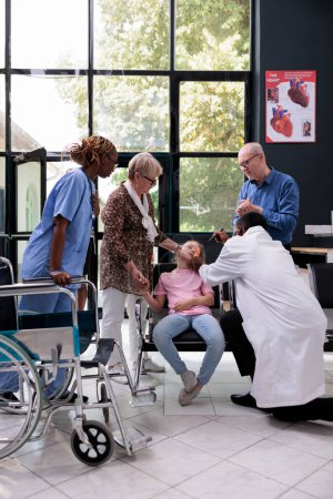Photo for Practitioner doctor helping unconscious child after fainting on chair in hospital reception during checkup visit consultation. Grandparents being worried trying to help granddaughter. Medicine service - Royalty Free Image