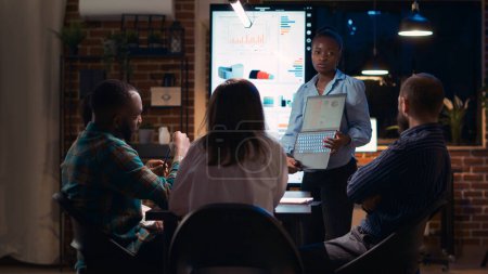 Téléchargez les photos : Employé afro-américain présentant un rapport, montrant des graphiques sur l'écran de l'ordinateur portable. Présentation de statistiques de recherche d'entreprise, équipe diversifiée discutant d'analyse, stratégie de vente de planification - en image libre de droit