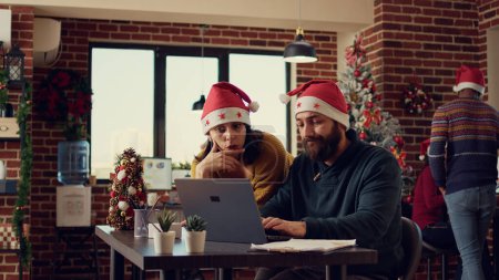 Photo for Office coworkers working on report in festive decorated space during christmas holiday season. Planning startup work on laptop and celebrating winter festivity with xmas decorations. - Royalty Free Image