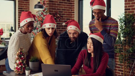 Photo for Multiethnic team of people brainstorming ideas in office with christmas tree and decorations. Diverse colleagues doing teamwork during winter holiday season celebration, festive ornaments. - Royalty Free Image