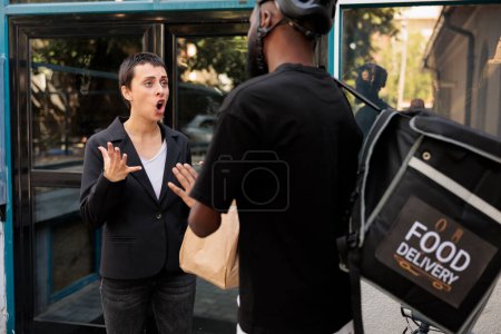 Photo for Food delivery delay, impulsive office employee getting wrong order. African american deliveryman giving angry upset customer takeaway meal in front of company building outdoors - Royalty Free Image