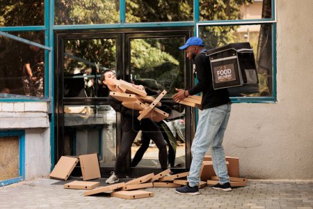 Photo for Shocked food delivery customer catching falling pizza boxes pile, confused courier dropping order in front of office building outdoors. Careless man delivering fastfood packages stack - Royalty Free Image