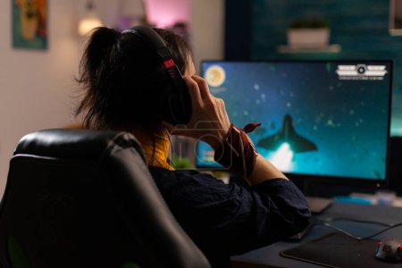 Foto de Mujer videogamer utilizando una poderosa computadora jugando videojuegos en línea en el estudio de juegos en casa. Transmisión virtual de auriculares cibernéticos que realizan torneos de juego con equipos profesionales. - Imagen libre de derechos
