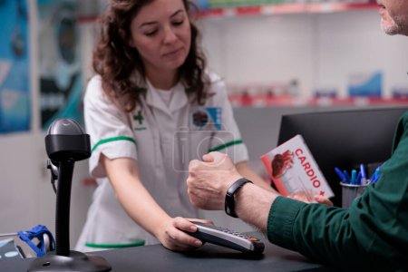 Photo for Elderly client paying cardiology pills with modern watch using terminal for contactless payment in drugstore. Customer buying pharmaceutical treatment to curse disease. Health care support - Royalty Free Image