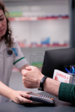 Photo for Senior client buying pharmaceutical treatment, doing contactless payment with modern watch in drugstore. Clients shopping supplements, vitamin for immune system. Close up - Royalty Free Image