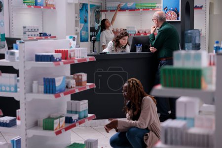 Foto de Cliente preguntando a farmacéutico para el consejo médico discutiendo sobre la prescripción de píldoras durante la consulta en farmacia. Estanterías de farmacias llenas de medicamentos, vitaminas y suplementos. Apoyo médico - Imagen libre de derechos