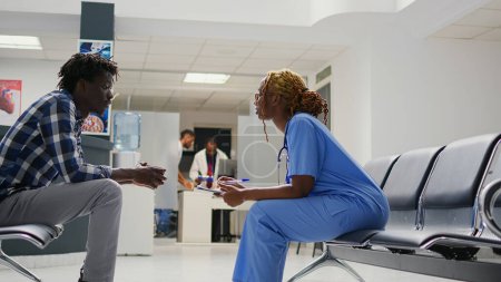 Photo for Medical staff doing examinations with african american people, patients with illness waiting in hospital lobby. Group of men sitting in waiting area before attending appointment. Tripod shot. - Royalty Free Image
