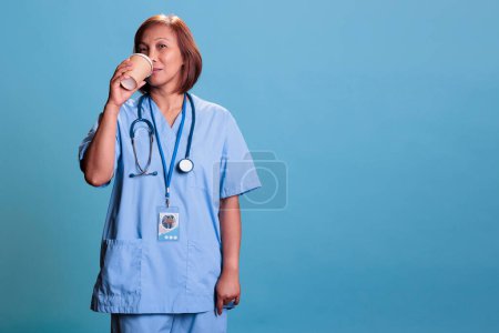 Téléchargez les photos : Portrait d'une infirmière asiatique âgée tenant une tasse de café avant la visite de contrôle rendez-vous, service de soins de santé. Médecin assistant médical travaillant à l'expertise de la maladie du patient. Concept de médecine - en image libre de droit
