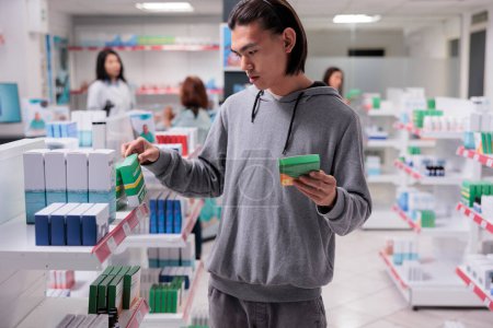 Foto de Hombre asiático cliente examinando suplementos en los estantes, cliente mirando las cajas de pastillas en la farmacia llena de productos de cuidado de la salud como vitaminas y medicamentos. Búsqueda de suministros médicos. - Imagen libre de derechos