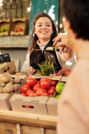 Propietario de la tienda de frutas y verduras ecológicas sonrientes que ofrece al cliente probar diferentes variedades de manzanas en el mercado de alimentos. Agricultora positiva vendiendo productos frescos locales de cosecha propia