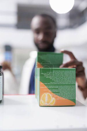 Photo for Pharmacy concept, african american pharmacist selling vitamins, taking pills from drugstore shelf, close up selective focus. Pharmaceutical service, medical supplement package - Royalty Free Image