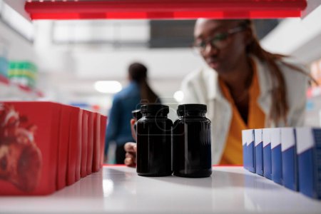 Photo for Pharmacist putting medication bottles on drugstore shelf, close up selective focus. African american woman taking pills packages, pharmaceutical service, medicaments selling - Royalty Free Image