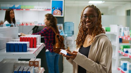 Photo for African american happy client checking packages of medicaments on drugstore shelves, buying healthcare products and vitamins in boxes at pharmacy. Person looking at pills and drugs. - Royalty Free Image