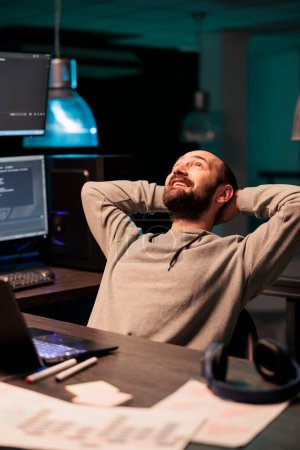 Téléchargez les photos : Ingénieur informatique joyeux relaxant sur chaise de bureau, finition cloud computing base de données. Se sentir heureux et détendu décontracté après avoir développé une nouvelle interface utilisateur, le succès de programmation de code. - en image libre de droit