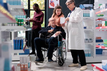 Téléchargez les photos : Travailleur de pharmacie âgé discutant du traitement médical avec le client handicapé, lisant la prescription médicale en pharmacie. Client en fauteuil roulant et soignant faisant des achats de médicaments pour guérir la maladie - en image libre de droit