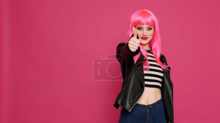 Photo for Stylish attractive person giving thumbs up on camera, expressing like and agreement symbol. Positive carefree woman showing okay and approval gesture, doing success sign in studio. - Royalty Free Image
