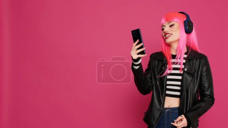 Téléchargez les photos : Modèle féminin tendance Hipster utilisant vidéocall conférence sur smartphone, parler aux gens sur la vidéoconférence en ligne. Cool fille élégante bavarder sur téléconférence à distance en studio. - en image libre de droit
