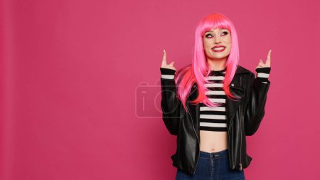 Photo for Stylish happy woman pointing up with fingers in studio, indicating upwards direction with raised arms. Beautiful cool person showing advertisement overhead or above, recommending directions. - Royalty Free Image