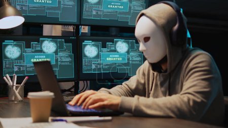 Maskierte Cyber-Diebe hacken nachts Computernetzwerk, arbeiten an Laptop und mehreren Monitoren, um IT-Informationen zu stehlen. Hacker mit versteckter Identität agieren gefährlich, Cloud Computing. Handschuss.