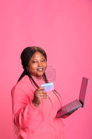 Foto de Mujer atractiva excitada insertando credenciales de tarjeta de crédito en el sitio de compras haciendo pago en línea en el estudio con antecedentes aislados. Modelo alegre que paga los productos en tienda digital - Imagen libre de derechos