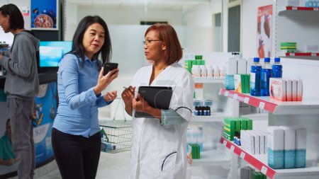 Photo for Medical consultant using digital gadget to do medicine inventory, analyzing pharmaceutical products on drugstore shelves. Woman working as pharmacist looking at pharmacy supplies stock. - Royalty Free Image