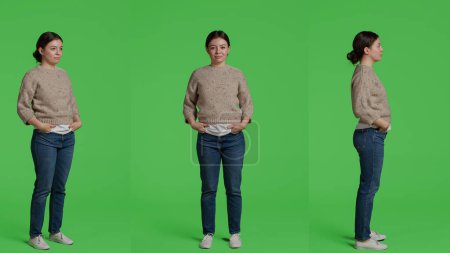 Photo for Female model posing on full body greenscreen backdrop, looking at camera and being cheerful. Young person acting friendly and confident in studio, standing over isolated green screen background. - Royalty Free Image