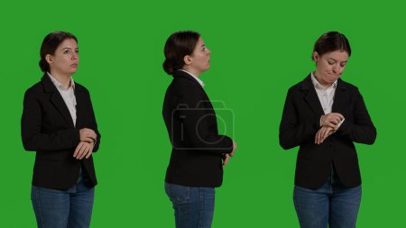 Téléchargez les photos : Close up of impatient office worker checking time on wristwatch, standing over isolated greenscreen backdrop. Young woman running late and looking at clock, waiting for something, - en image libre de droit