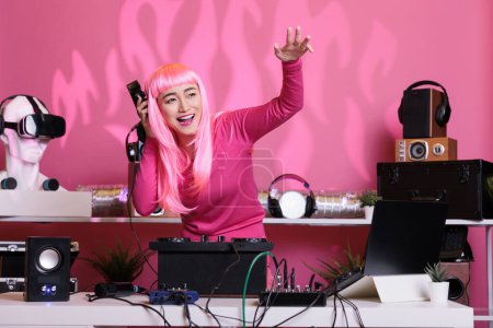 Photo for Artist with pink hair having fun while performing eletronic music in night club playing song using professional turntables. Woman standing at dj table dancing while celebrating album with fans - Royalty Free Image