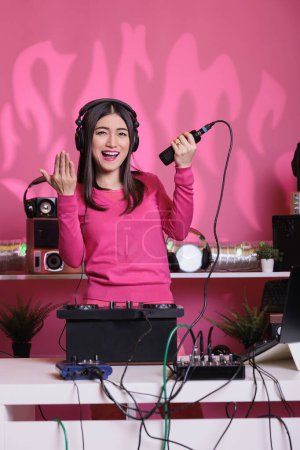 Téléchargez les photos : Happy musician having fun while playing eletronic music using professional mixer console in studio over pink background. Musical artist performing sounds to produce melody at turntables - en image libre de droit