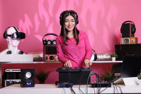 Foto de Asian musician mixes electronic techno sounds, wearing headphones at DJ table in club. Performing live, using turntables for an unforgettable concert experience. Surrounded by fans at the party - Imagen libre de derechos