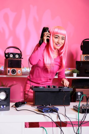 Téléchargez les photos : Asian dj mixing electronic music on turntables while playing record mix sounds in studio with pink background. Performer having fun while performing techno song, enjoying night lifestyle - en image libre de droit