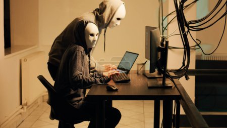Téléchargez les photos : Hackers with white masks hacking network to steal passwords directly from government system, cyberattack. Masked cyber spies using computer malware to break into web software. - en image libre de droit