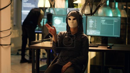 Hackerin mit anonymer Maske, die Hologramm verwendet, um in die Firewall-Verschlüsselung einzudringen, holografisches illegales Hacker-Konzept. Maskierter gefährlicher Dieb nutzt Augmented Reality, um System zu hacken.