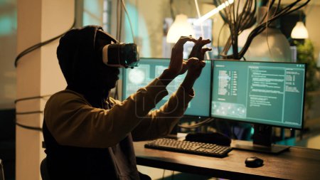 Téléchargez les photos : Male cyber criminal hacking network system with vr headset, using virtual reality to steal passwords and info illegally. Young adult using hacktivism skills to break into security server. - en image libre de droit