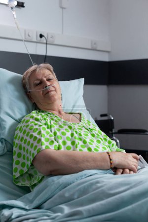 Téléchargez les photos : Old lady resting on bed at hospital room. Elderly woman sedated for surgery in clinic. Senior female resting, sleeping, recovering from infection. Patient with disease using medical aid for breathing. - en image libre de droit