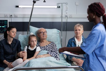 Téléchargez les photos : Surgeon filling out necessary paperwork to admit sick elderly man for medical intervention at operating room. Chronically ill grandfather being cared by african american doctor. - en image libre de droit
