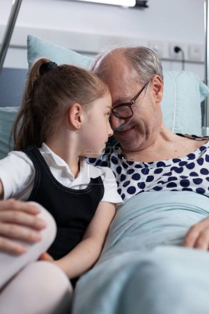 Téléchargez les photos : Hospitalized grandfather surprised, happy by little granddaughter unexpected visit in hospital observation room. Girl showing physical affection, hugging elderly sick man in geriatric clinic. - en image libre de droit