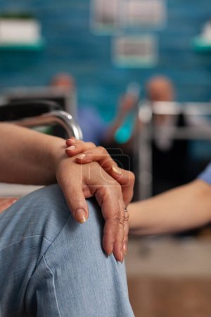 Téléchargez les photos : Female senior resident in wheelchair receiving specialized care from a trained medical assistant. Professional nurse giving support to a patient with a disability in waiting room of a nursing home. - en image libre de droit