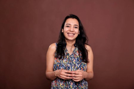 Foto de Smiling indian woman intertwining fingers portrait, laughing, looking at camera. Positive lady, young person standing with cheerful facial expression, front view studio mid shot - Imagen libre de derechos
