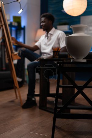 Photo for Artistic young man making artwork in home drawing studio with creative tools. Close up of vase used to create pencil masterpiece. Young african american artist sketching on easel at atelier. - Royalty Free Image