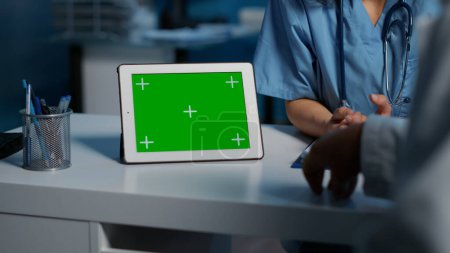 Photo for Nurse showing tablet computer with green screen display to doctor while discussing medical expertise during checkup visit. Clinical staff working late at night in hospital office - Royalty Free Image