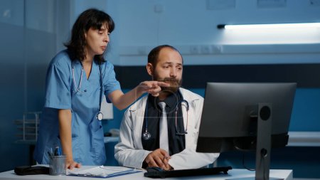 Photo for Medic and nurse analyzing patient medical report discussing disease symptoms working over hours at health care treatment during checkup visit in hospital office. Medicine service and concept - Royalty Free Image