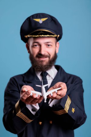 Foto de Portrait of airplane aviator in uniform holding plane toy in palms front view, pilot playing with commercial passenger jet model . Professional aviation academy aviator on blue background - Imagen libre de derechos