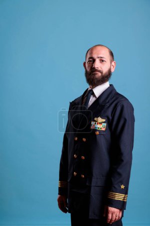 Photo for Airplane captain standing in professional uniform portrait, confident plane pilot standing, looking at camera, studio medium shot, side view. Civil aviator with badge on jacket - Royalty Free Image